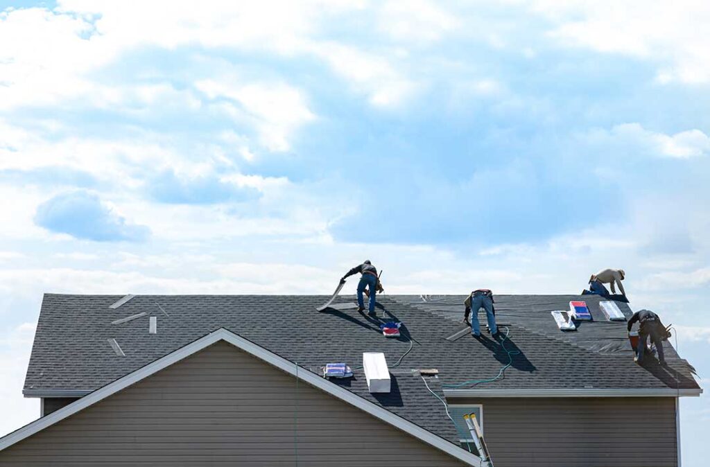 A roofer carefully unrolls synthetic underlayment across wooden roof decking on a sunny day.
