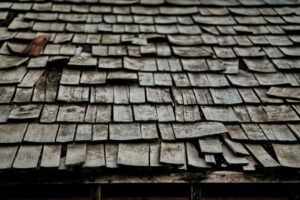 An attic view showing wood roof decking, rafters, insulation, and a small water stain near a roof penetration